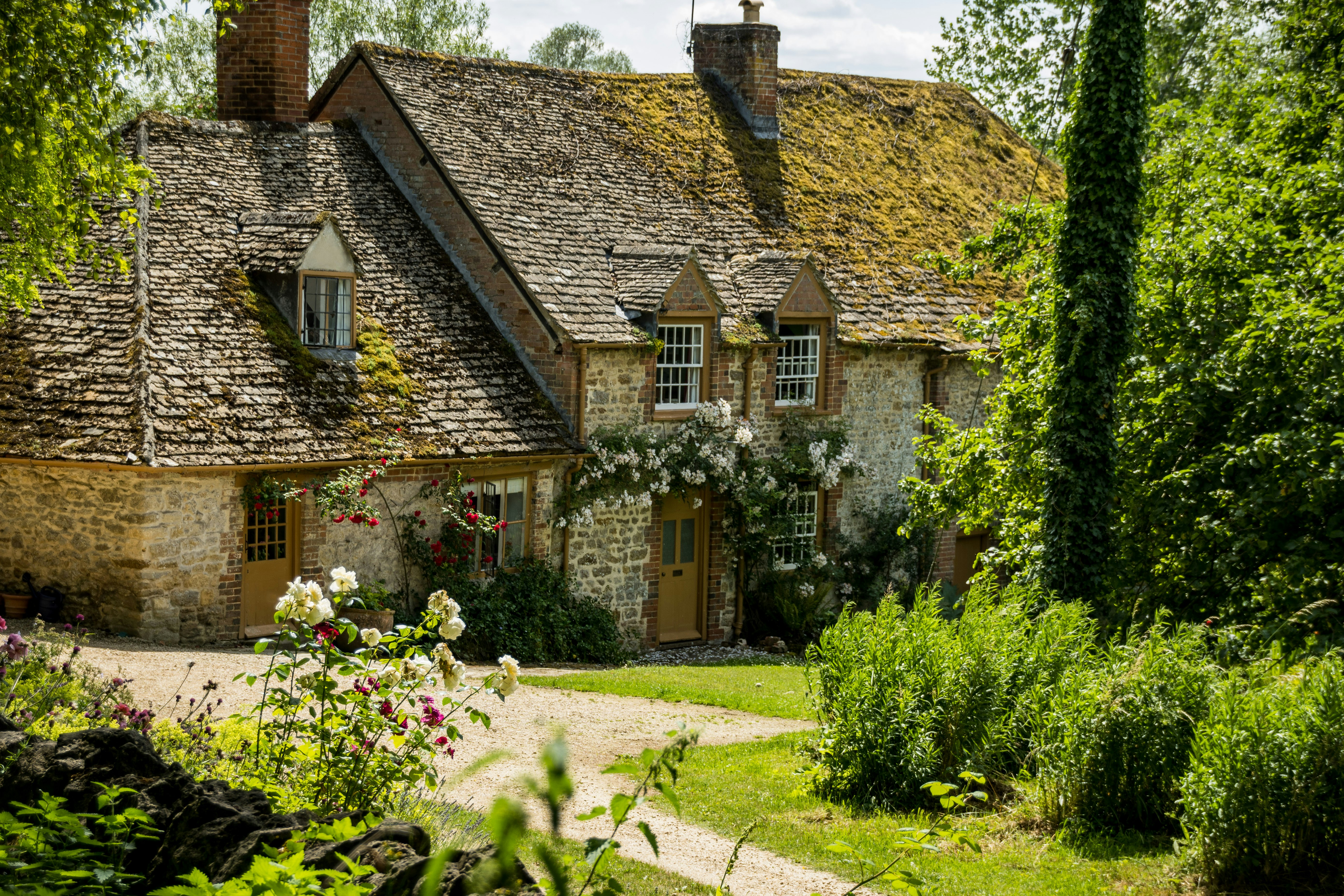 A stone cottage with a green roof surrounded by greenery in the Cotswolds, England